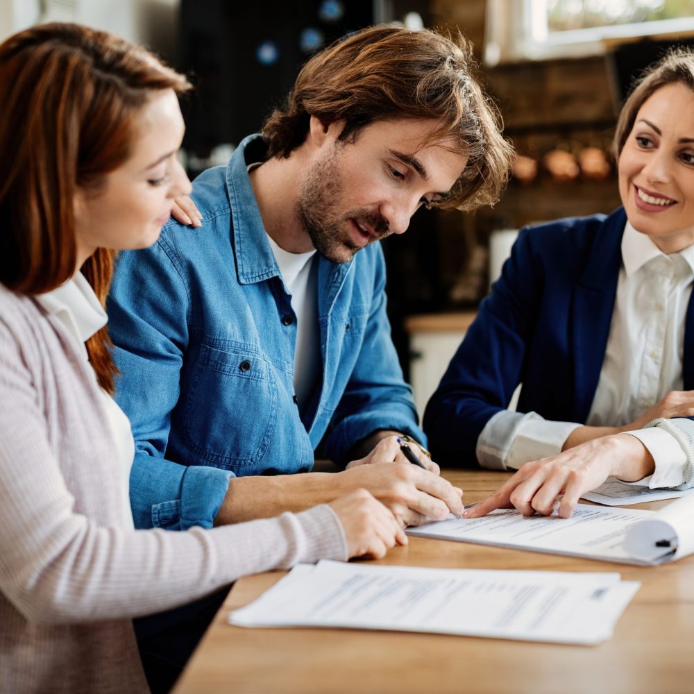 Young couple signing a contract on a meeting with financial advi Young couple signing lease agreement while having meeting with real estate agent. Focus is on man.